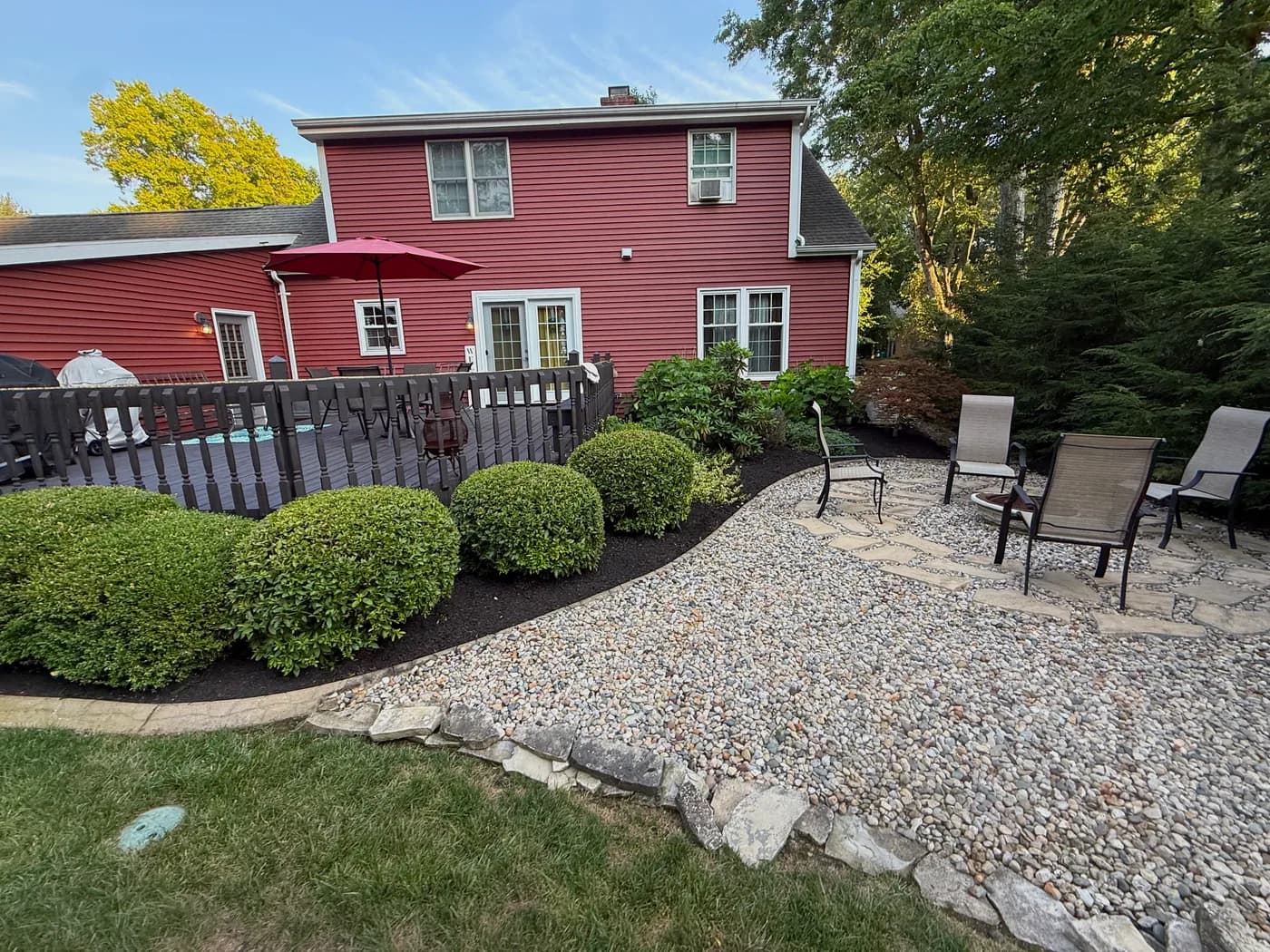 River-rock patio and trimmed shrubs behind a red colonial home